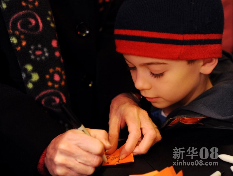 12月29日，在美国纽约时报广场的心愿墙前，一个男孩在看自己母亲填写心愿纸片。新华社照片，纽约，2011年12月29日 新华社记者申宏摄  2012年来临之际，纽约时报广场咨询中心内专门设立了一面心愿墙，来自世界各地的游客都可以将写有自己新年美好心愿的五彩纸片贴到上边。所有的纸片将被收集起来，在2012年新年钟声敲响之际，从时报广场上空飘散而下。 