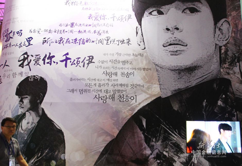 6月9日，在韩国首尔，一名工作人员从《来自星星的你》展览上的照片墙前经过。新华社记者姚琪琳摄  