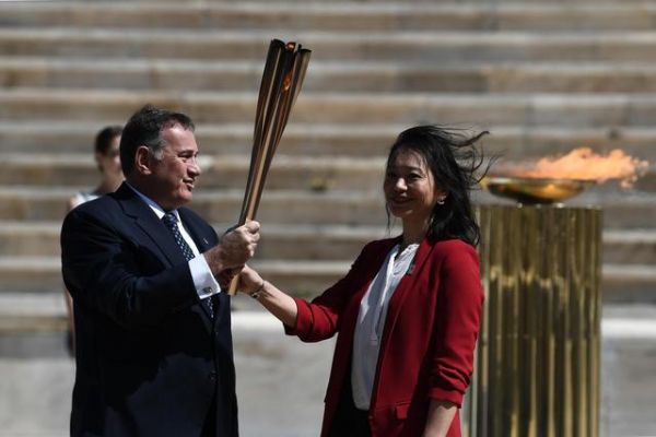 3月19日，日本代表团成员井本直步子（右）从希腊奥委会主席斯皮罗斯·卡普拉洛斯手中接过东京奥运会圣火
